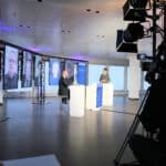 Hybrides Event mit Moderatoren im Studio und mehreren Teilnehmern auf großen LED-Bildschirmen, professionell umgesetzt mit Eventtechnik.