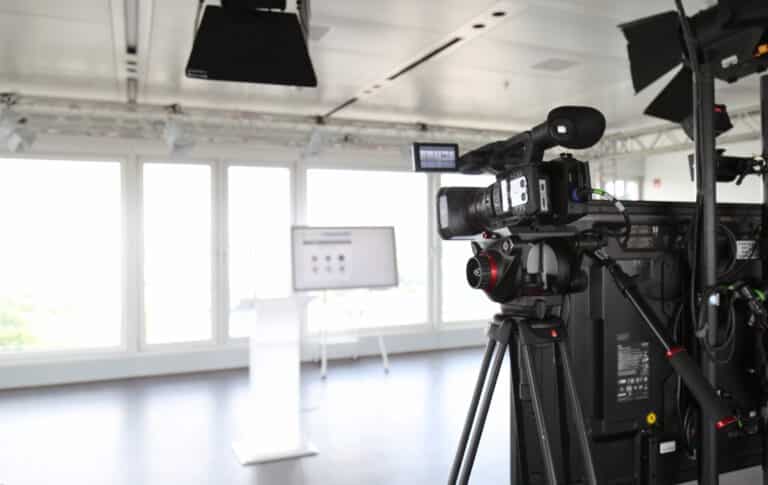 Professionelle Kamera auf Stativ für die Aufzeichnung und Live-Übertragung von Hybrid Events, ergänzt durch Studio-Lichttechnik.