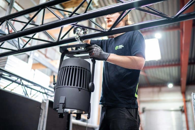 ETnord-Techniker montiert einen Scheinwerfer an einer Traverse, im schwarzen Shirt der EventTechnik nord mit Arbeitshandschuhen