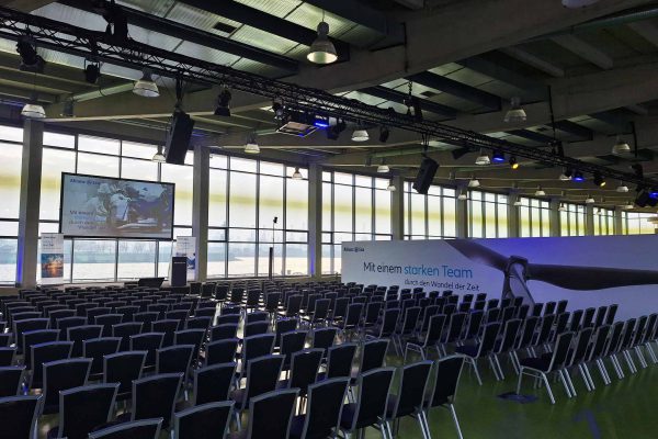 Reihenbestuhlung vor einer Bühne mit Rednerpult, Leinwand und Eventtechnik in einer Eventlocation