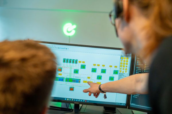 Zwei Personen betrachten einen Bildschirm mit einem technischen Schaltplan, eine davon zeigt erklärend auf bestimmte Elemente.