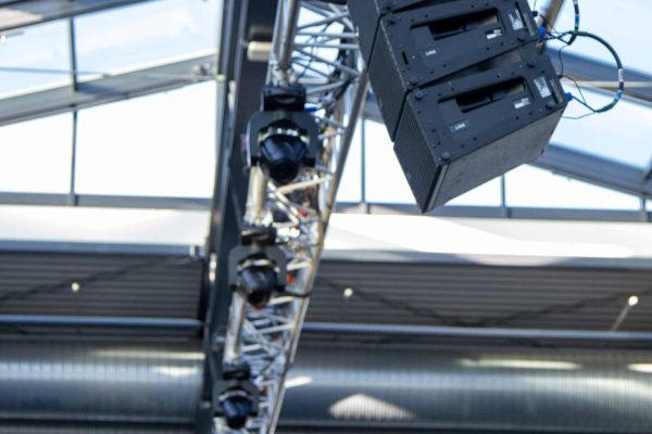 Aufgehängtes Line-Array-Lautsprechersystem und Scheinwerfer an einer Traverse unter einem Glasdach, installiert für die Beschallung einer Veranstaltung