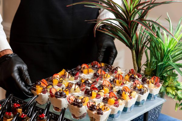 Primär: Mini-Burger mit Sesambrötchen auf einer weißen Catering-Platte, einer davon mit Holzspieß und Kennzeichnung „Vegan"