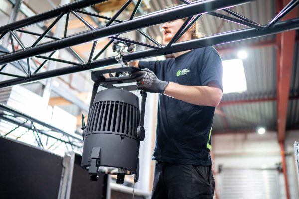 ETnord-Techniker montiert einen Scheinwerfer an einer Traverse, im schwarzen Shirt der EventTechnik nord mit Arbeitshandschuhen