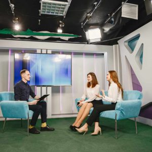 Tv host on talk show with two women guests Female guests are sitting on sofa.Journalist taking interview. Morning show.